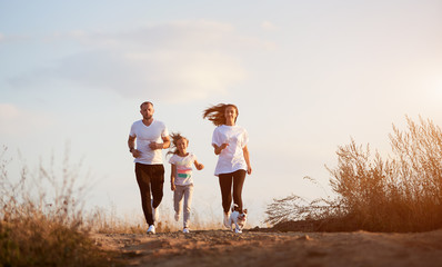 Front view of young and beautiful family of three jogging with their dog outside the city on the...