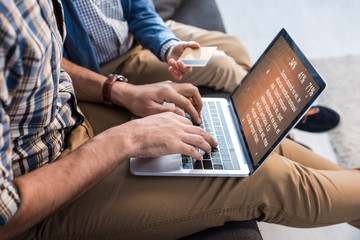 cropped view of jewish father using laptop with website and son holding credit card