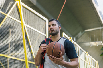 Closeup of a handsome and attractive male athlete of Latin origin, carrying his basketball while walking down the street