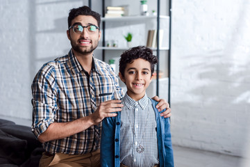smiling jewish father hugging son and looking at camera in apartment
