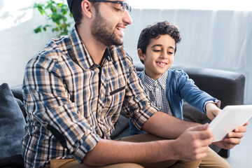 smiling jewish father and son using digital tablet in apartment
