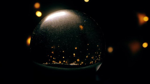 Christmas snow globe animation on hand. A garland of lights glows in the background.