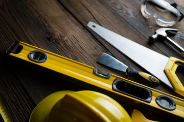 Contractor concept. Yellow hardhat, libella and other tools on the rustic wooden background.