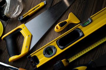 Contractor concept. Yellow hardhat, libella and other tools on the rustic wooden background.