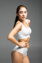 Young beautiful woman body on gray background in white sport clothes