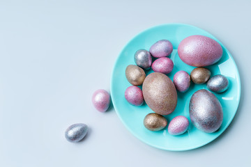 Colored painted pearl chicken and quail eggs of pink, silver, golden color on a blue mint plate pastel background. Minimalistic creative neo easter festive vertical flat lay. Copyspace for text