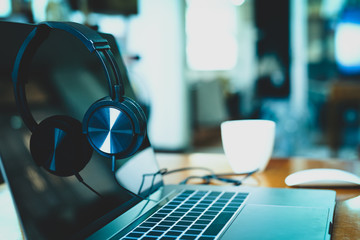 Headphones on laptop with coffee cup and mouses in blur background.