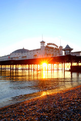 Brighton Palace Pier glowing yellow with the sun setting underneath it reflecting on a calm sea
