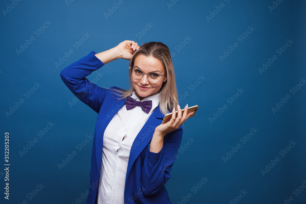 Wall mural Cute and funny businesswoman in a stylish blue jacket and bow tie uses a smartphone.