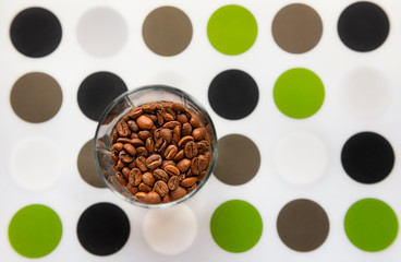 Composition with glass of coffee beans on coloured dots mat
