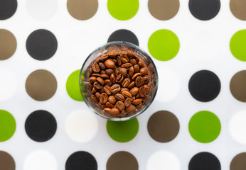 Composition with glass of coffee beans on coloured dots mat