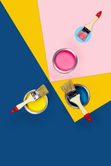 Renovation concept. Tricolor blue, yellow, pink background with three paint jars and brushes. Flat lay, top view, copy space.