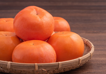 Fresh, beautiful orange color persimmon kaki on bamboo sieve over dark wooden table. Seasonal, traditional fruit of Chinese lunar new year, close up.