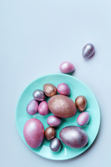 Colored painted pearl chicken and quail eggs of pink, silver, golden color on a blue mint plate pastel background. Minimalistic creative neo easter festive vertical flat lay. Copyspace for text