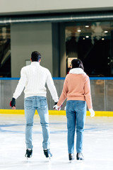 back view of young couple holding hands on skating rink