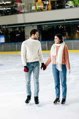 beautiful smiling couple holding hands on skating rink