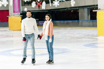 smiling young couple holding hands on skating rink