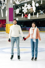 smiling young couple holding hands while skating on rink