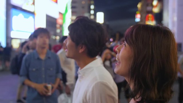 Dating couple walking across famous Dotombori bridge in Osaka Japan at nihgt neon lights