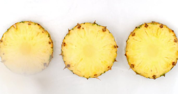 Top view: 3 slices of pineapple washed with water on a white background. Water splashes in slow motion