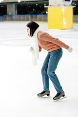 beautiful girl in sweater and scarf skating on rink