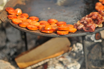 Sausages on the side of a pan on a campsite