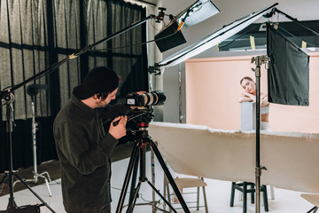 Cameraman shooting attractive model in photo studio with spotlights