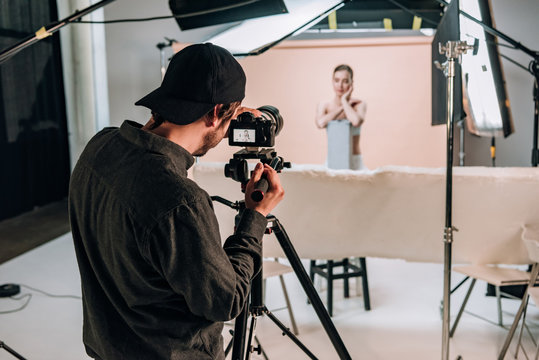 Selective focus of cameraman filming beautiful model in photo studio with spotlights
