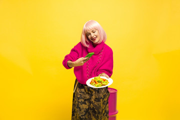 It's hard to be influencer. Selfie first, eating later. Need shot a dish before. Caucasian woman's portrait on yellow. Beautiful blonde model. Concept of human emotions, facial expression, sales, ad.
