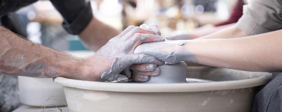 Craftsman teaching girl how to  throw clay vessel on pottery wheel