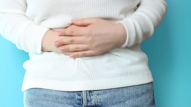 Girl holding her belly on blue background, concept of acute pain, blue background