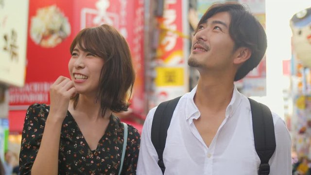 Fun classy Japanese couple explore Osaka food street bright lights background sense expereience