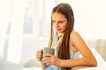 portrait of young teenager brunette girl with long hair sitting on sofa with cup at home