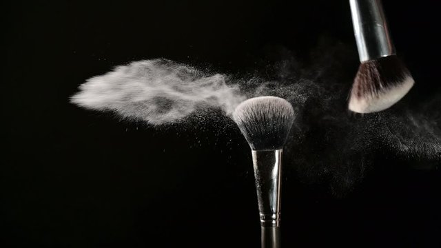Makeup artist hit brush to create blow of powder over black background