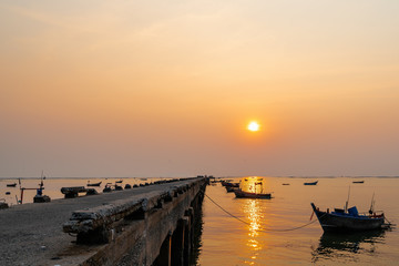 Beautiful seascape sunset with silhouette fishing wood boat floating down on sea at jetty in asia