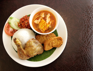 Fried chicken rice served with fried tofu, fried tempeh and tamarind vegetables on a leather table