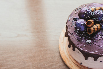 Purple glitter blueberry cake with chocolate glaze on a wooden table copy space. Homemade chocolate cake with blueberries and striped wafer rolls.