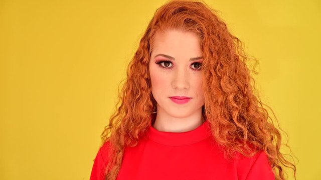 Portrait of beautiful readhead woman in red dress over yellow background
