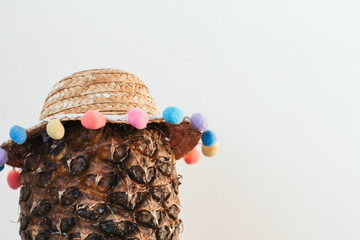  Ripe pineapple in a summer straw hat with colored pompons copy space.