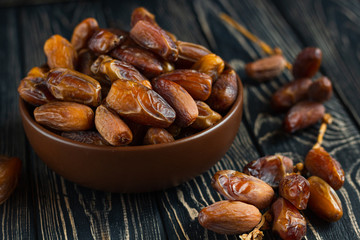 Sweet dessert dried date in brown ceramic bowl on an old dark wooden table. Low key, selective focus. Delicious ingredient for vegan dessert. Close up