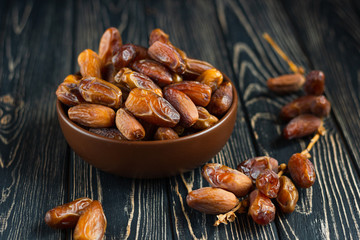 Sweet dessert dried date in brown ceramic bowl on an old dark wooden table. Low key, selective focus. Delicious ingredient for vegan dessert. Close up