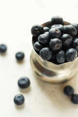 Iron bowl with fresh ripe blueberries on a white table in high key. Close up, selective focus