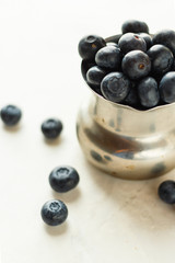 Iron bowl with fresh ripe blueberries on a white table in high key. Close up, selective focus