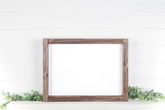 Mock up A4 horizontal frame made of rough wood with on a shelf with greens
