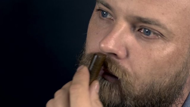white bearded hipster man combing his beard with a comb