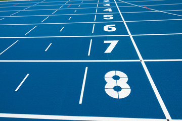 Blue running treadmill track with lane numbers in stadium outdoors