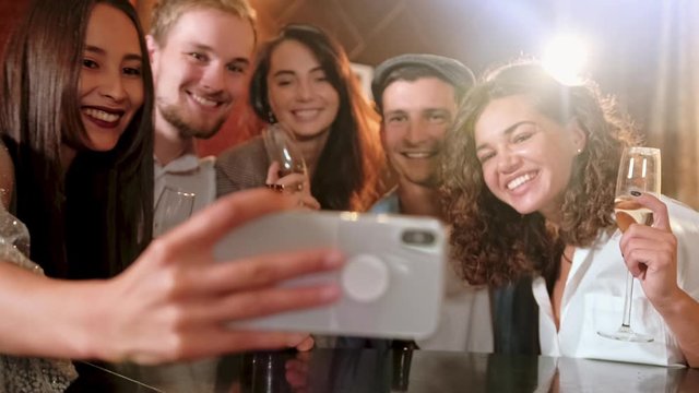 Young Cheerful Female Friends Taking Selfie In Pub Using Phone. Friends, men, women, leisure, friendship and technology concept - friends with smartphones drinking beer at bar or pub