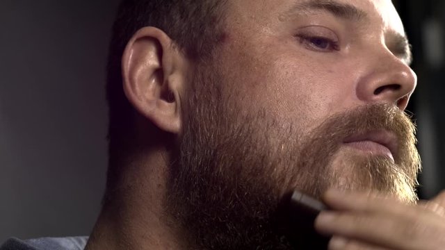 white bearded hipster man combing his beard with a comb
