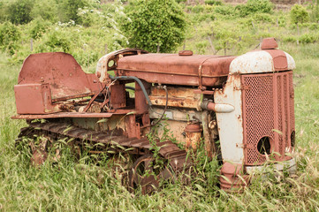 Old neglected rusty small vintage caterpillar tractor on green meadow