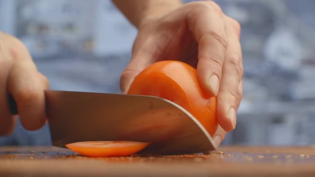 Closeup of a woman cutting and chopping tomato by knife on wooden board.